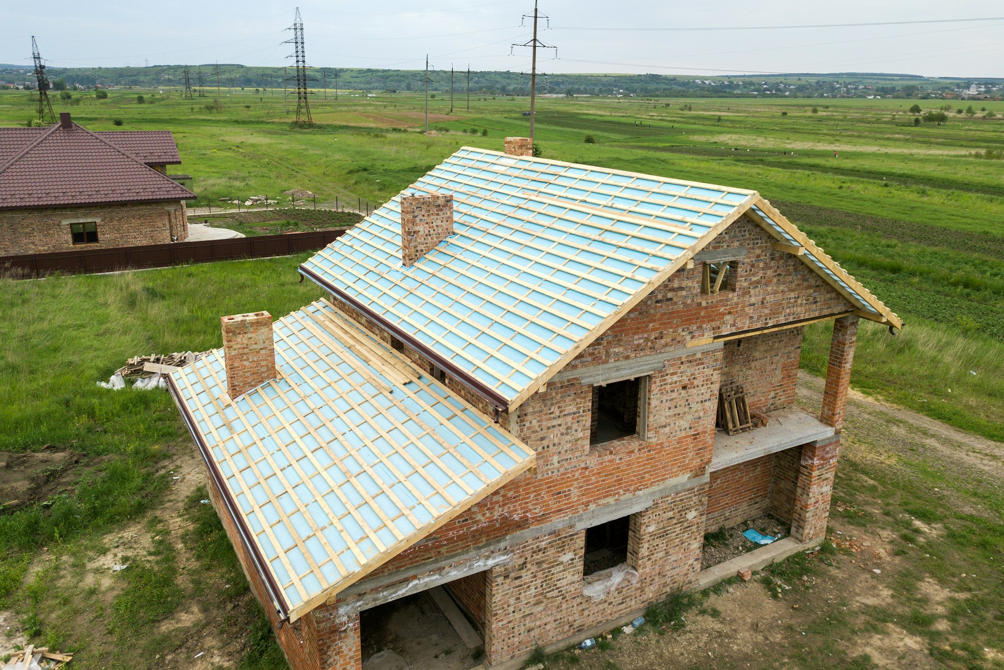 Aerial view of a brick house with wooden roof frame under construction.