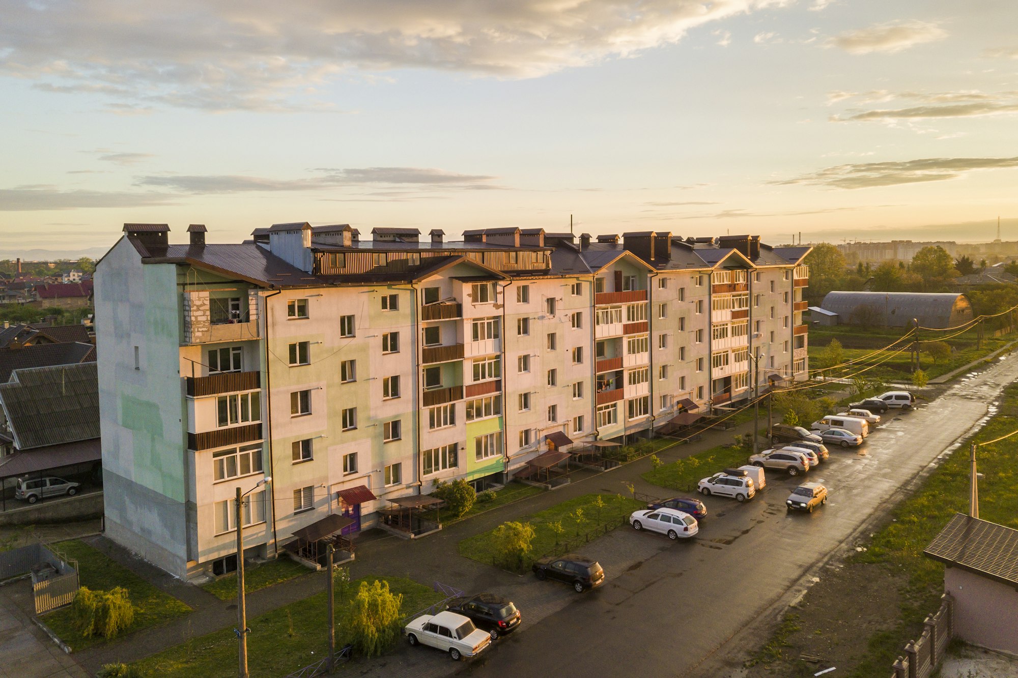 Suburb landscape, apartment building. Parked cars along bad road on spring day